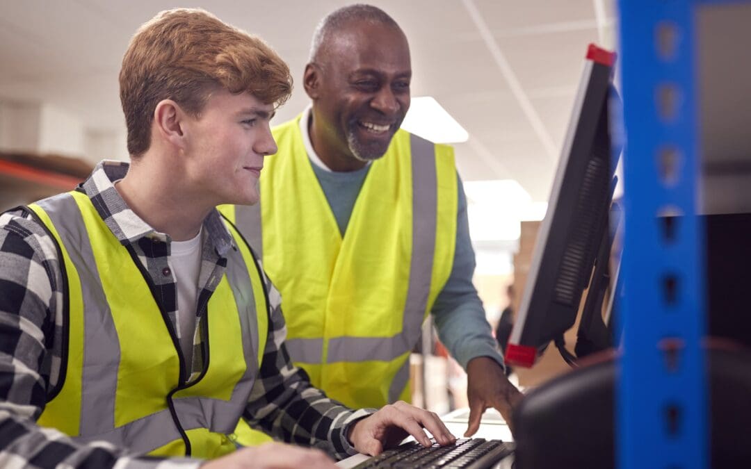 Intern With Supervisor Working In Warehouse On Computer Terminal